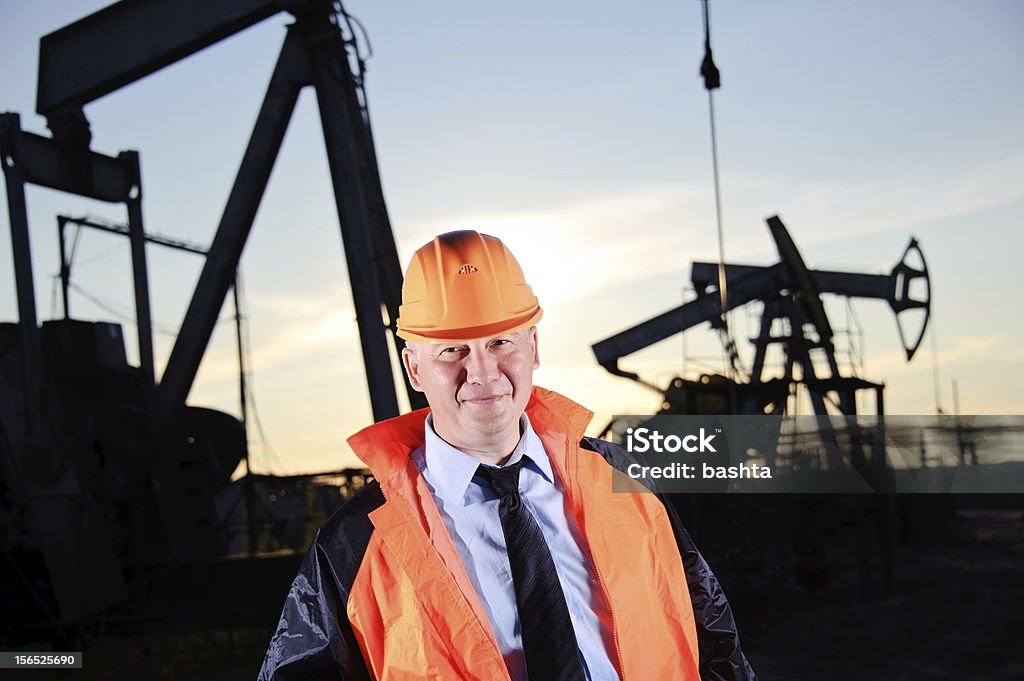 Engineer in an Oil field Oil worker in orange uniform and helmet on of background the pump jack and sunset sky. Adult Stock Photo