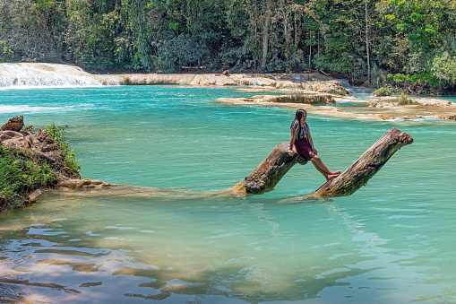 Indigenous maya lady on wooden branch along the cascades of Agua Azul with rainforest, Chiapas, Mexico.