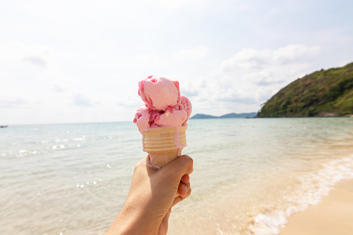 Hand holding ice cream cone on the beach in summer day.