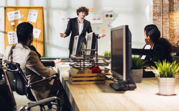 istock Selective focus young handsome smart Caucasian Businessman or boss wearing suit, smiling with happiness, confidence, presenting marketing plan or creative idea in meeting room at indoor modern office. 1565297420