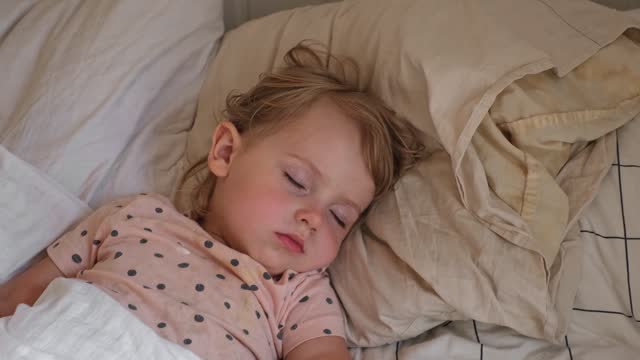 Peaceful adorable baby sleeping on a bed at home. Slumbering little child. Two year old girl sleeps peaceful at domestic room interior background. Serene dream. Cute face close up. Deep kid slumber