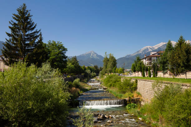 View of Bansko town, bulgarian ski resort in summer, Pirin Mountains on the background, a river on the foreground, Bulgaria. View of Bansko town, bulgarian ski resort in summer, Pirin Mountains on the background, a river on the foreground, Bulgaria. bulgarian culture bulgaria bridge river stock pictures, royalty-free photos & images