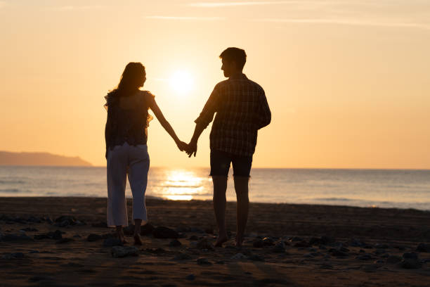 istock Couple walking along coastline during sunset holding hands 1565383605