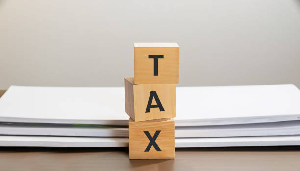 istock TAX on wooden cube with stack of papers with documents 1565403338