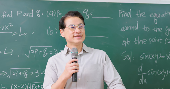 asian senior male confident calculus professor is teaching in front of blackboard with microphone at college classroom