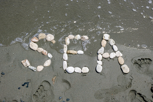Word Sea made of white pebbles on wet beach sand among footprints