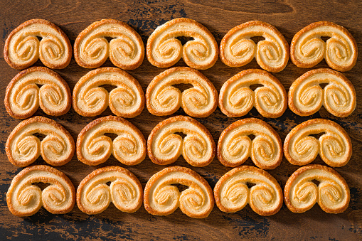Palmiers, baked elephant ear puff pastry cookies in a row pattern on wooden background board table