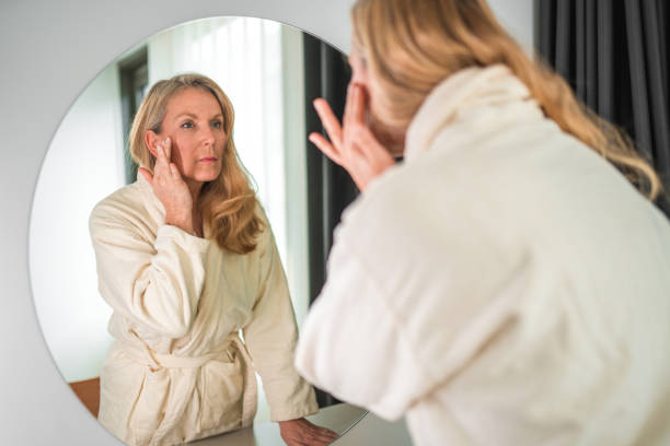 istock Lovely Mature Caucasian In A Bathrobe Looking At A Mirror 1565500932