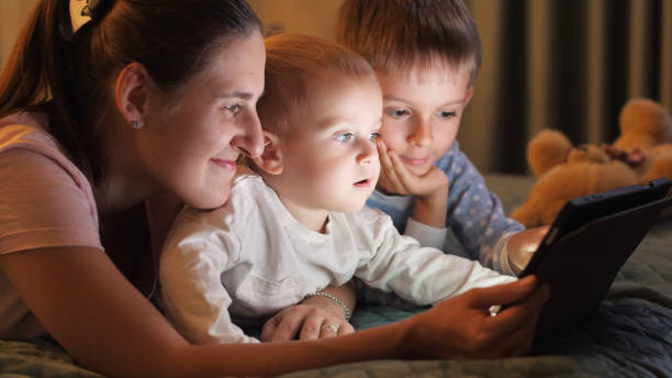 istock Two smiling brothers in pajamas playing on tablet computer with mother before going to sleep. Family having time together, parenting, happy childhood and entertainment. 1565519874
