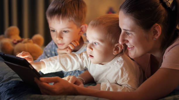 istock Young mother lying with two boys in bed playing on tablet computer at night. Family having time together, parenting, happy childhood and entertainment. 1565520397