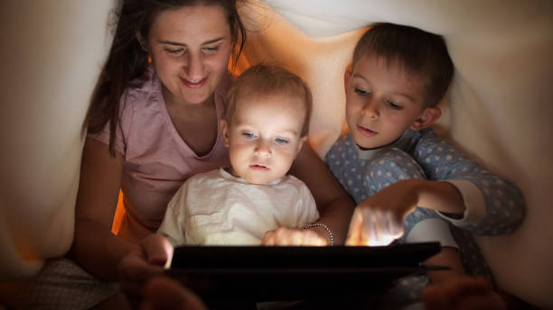 istock Happy cheerful family hiding under blanket and using tablet computer. Family having time together, parenting, happy childhood and entertainment. 1565520434