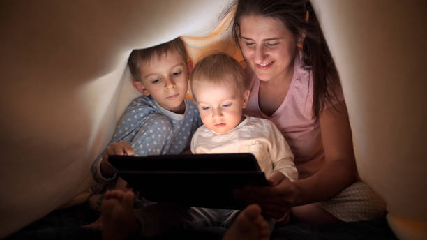 istock Happy family in pajamas browsing internet and watching video on tablet computer in bed under blanket. Family having time together, parenting, happy childhood and entertainment. 1565520943