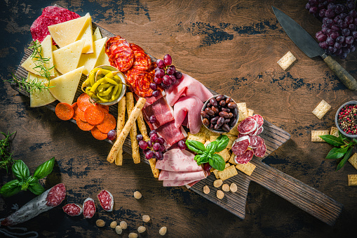 Mediterranean appeticer antipasto, on rustic wooden board with cold cuts meat charcuterie slices, manchego cheese, pepperoni, chopped, ham,  prosciutto and chorizo with bread sticks, crackers olives and pickles