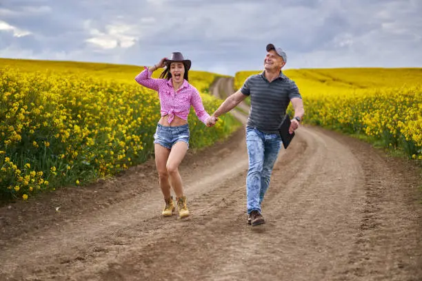 Happy farmers couple on a funny stroll through a canola field