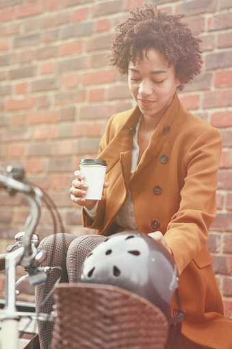 Woman sitting on a bench and drinking coffee. Her bicycle and helmet by her.