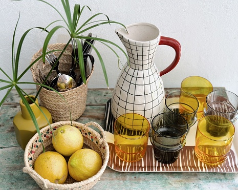 Still life with ceramic jug, crystal glasses, basket with lemons and green plant