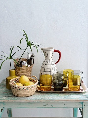 Still life with ceramic jug, crystal glasses, basket with lemons and green plant