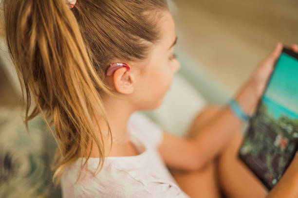 GIRL WITH HEADPHONE USING TABLET Girl with a hearing aid on the sofa using a tablet assistive technology stock pictures, royalty-free photos & images