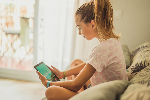 Girl with a hearing aid on the sofa using a tablet