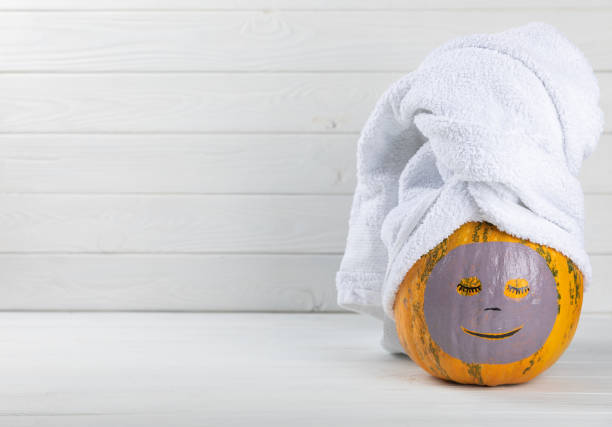 istock Pumpkins with face mask and towel on white background, burning candle, cosmetics with copy space 1565678943