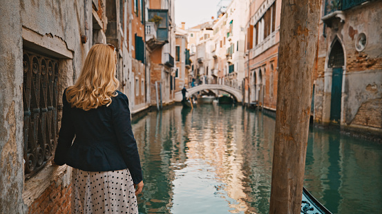 Blond mid adult woman examining canal while standing by building  during vacation