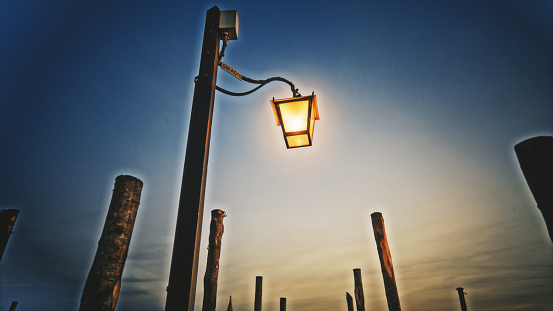 Illuminated electric lamp amidst wooden poles against sky during dusk