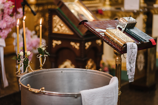 Baptism water and can. Baptismal font with candles and jug. Christening in the baptismal font in the Ukrainian Orthodox Church. Closeup.