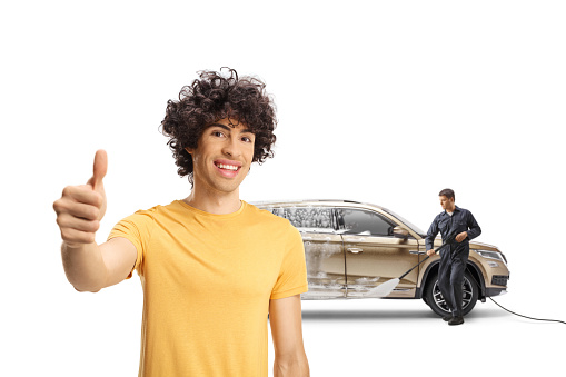 Happy young man with a SUV gesturing thumb up sign at a carwash isolated on white background