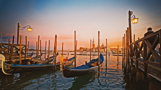 Gondolas moored near jetty over sea with Church of San Giorgio Maggiore in background under sky during sunset