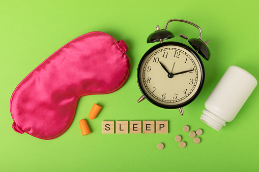 Sleeping mask, alarm clock, insomnia pills and ear plugs on a background. The concept of rest, sleep quality, good night, insomnia and relaxation. View from above. flat lay