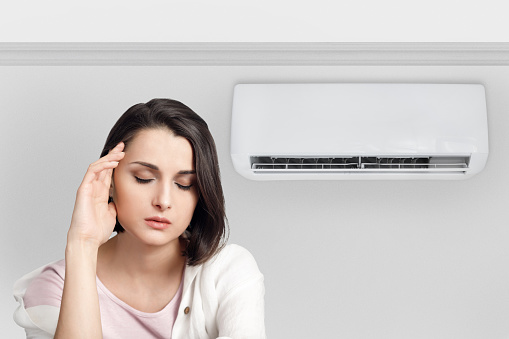 Woman holding her head while experiencing a cold and feeling unwell due to the air conditioner.