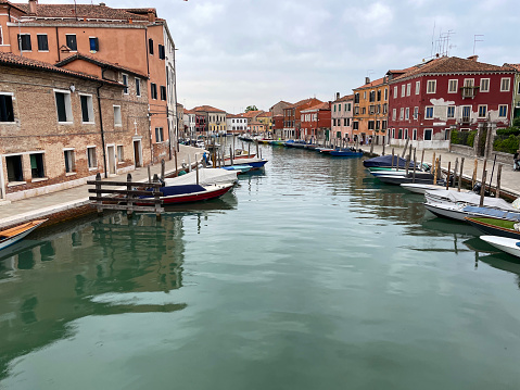 Stock photo showing view from a bridge looking along a canal lined with colourful buildings and moored boats in Murano, Venice, Italy. Famous for glass making, Murano is a group of islands, in the Venetian Lagoon, joined by bridges.
