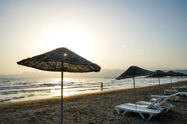 istock People walks on beach at sunset, sunbed, beach parasol 1565715354