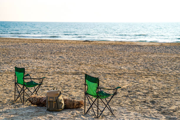 istock Folding green camping chair on the beach, palm tree block and mountaineer backpack 1565717610