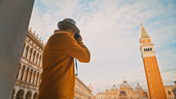 istock Man exploring while taking picture of Campanile and Saint Mark's Basilica through camera at San Marco square 1565721023
