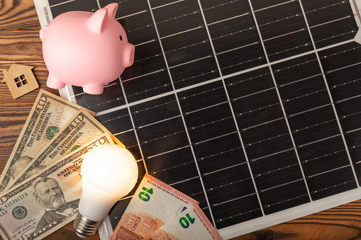 Flat lay composition with solar panel, led lamp and piggy bank on background. The concept of saving money and clean energy. The concept of ecology and sustainable development.