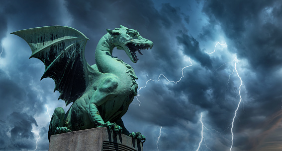View of the Dragon bridge (Zmajski most), symbol of Ljubljana, capital of Slovenia, Europe. Sculpture of a dragon against a dark stormy sky.
