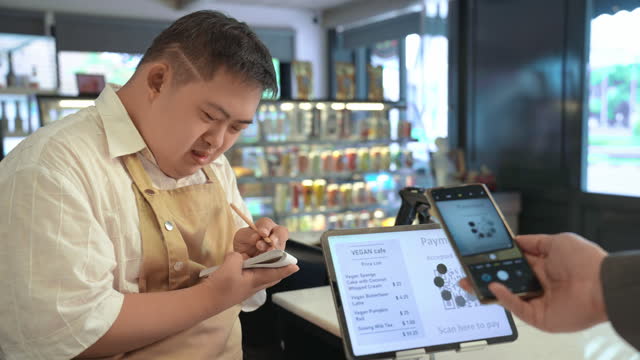 A customer buying a delicious coffee from supermarket and paying money by using a smart phone to young Asian man with disability. Contactless payment. Paying with online banking from application. Contactless technology.