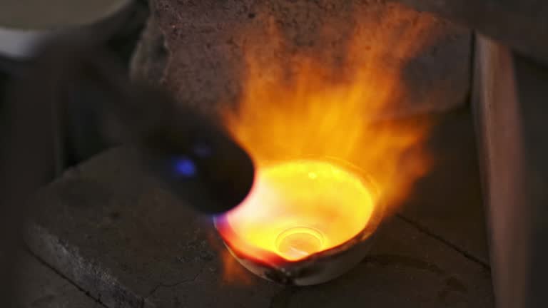 A craftsman jeweler is melting some silver jewels with a blowtorch