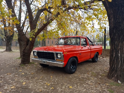Remedios de Escalada, Argentina – July 10, 2023: Old red utility 1979 Ford F 100 V8 pickup truck under the trees. Classic car show.