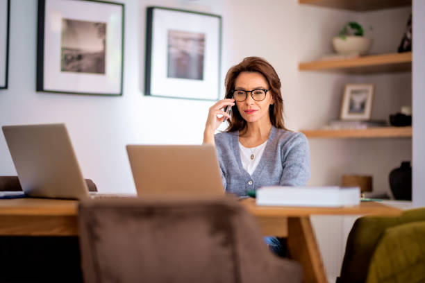 istock Mid aged business woman sitting at home and using laptops and having a call 1565874111