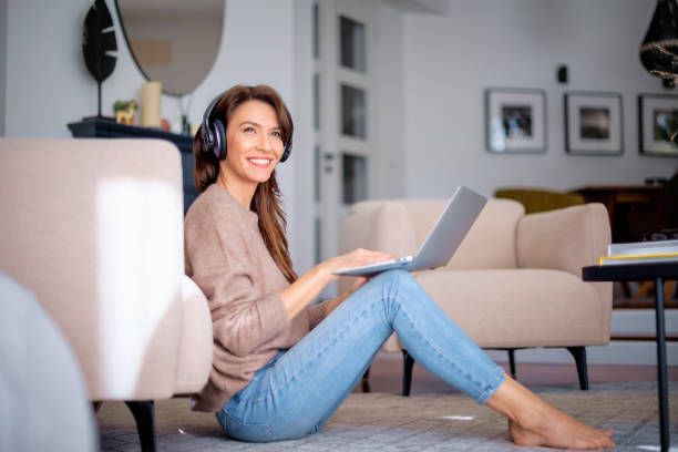 istock Full length of middle aged woman with headphone using a laptop while browsing on the internet at home 1565874653