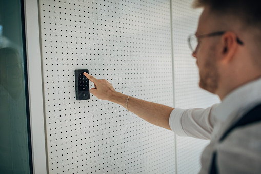 A young handsome businessman arrives at work. He enters the pin code to enter the company.