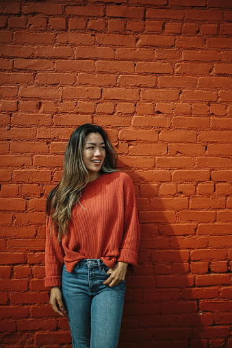 Stylish Asian - American woman walking on the streets of Los Angeles, California, in Van Nuys area of the Valley, against the brick wall.