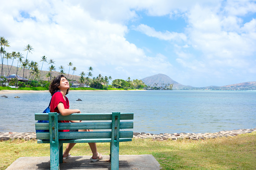 Young woman resting on park bench along Hawaiian ocean, Kokohead Crater in background
