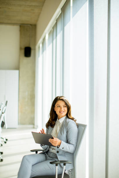 istock Young woman working on digital tablet by the office window 1565959343