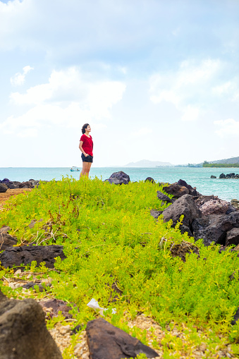 Young woman standing on grassy hill looking out over  Hawaiian ocean