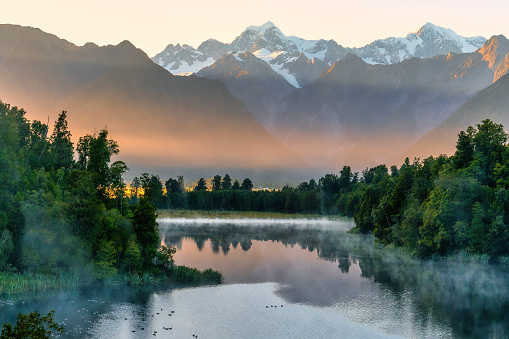 First early morning light of the day at the beautiful Lake Matheson  on the West Coast with some mist rising around the lakeshore