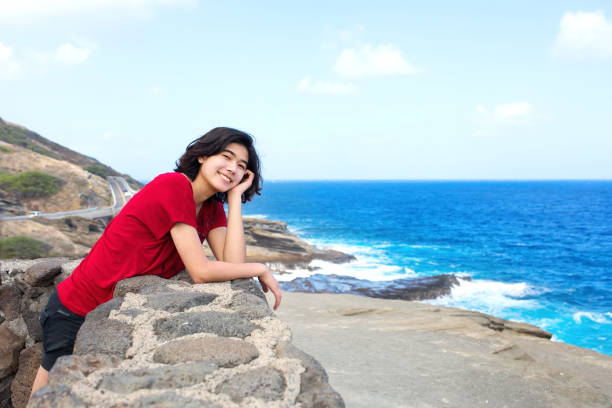 istock Young woman leaning against stone wall overlooking Hawaiian ocean 1566001022
