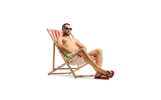 Fit man in swimwear sitting on a beach chair isolated on white background